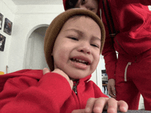 a little boy wearing a red jacket and a brown beanie