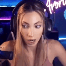 a woman wearing headphones and a pink tank top is sitting in front of a computer screen .
