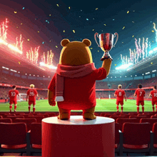 a teddy bear is holding a trophy in front of a soccer field