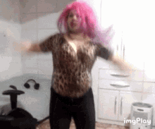 a woman wearing a pink wig and a leopard print shirt is dancing in a kitchen ..