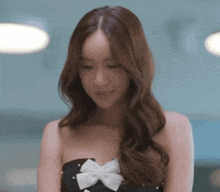 a woman in a black strapless dress with a white bow is smiling .