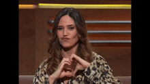 a woman is making a heart shape with her hands while sitting on a couch .