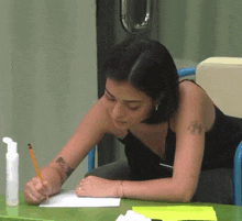 a woman with a tattoo on her arm writes on a piece of paper with a pencil