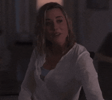 a woman in a white shirt is smiling in a dark room .