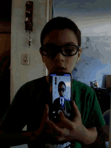 a boy wearing glasses is taking a picture of himself on a cell phone
