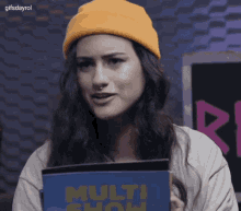 a woman wearing a yellow beanie is holding a book titled multi show