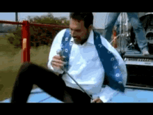 a man singing into a microphone while sitting on a blue car