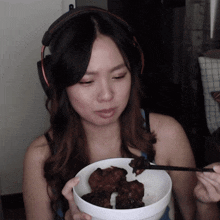 a woman wearing headphones is holding a bowl of food with chopsticks