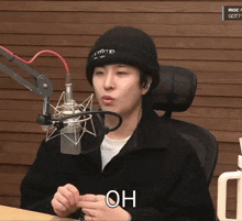 a man wearing a black beanie is sitting in front of a microphone with the word oh above his head