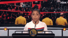 a woman stands behind a podium that says nick on the bottom