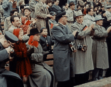 a crowd of people in trench coats and hats are clapping their hands