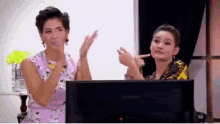 two women are clapping in front of a lenovo monitor