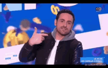 a man in a black jacket is giving a thumbs up on a television screen .