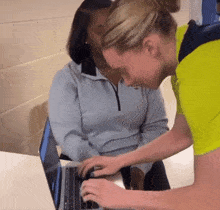 a woman in a yellow shirt is helping another woman use a laptop