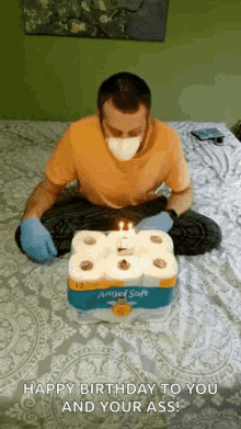 a man wearing a mask and gloves is sitting on a bed with a birthday cake made out of toilet paper .