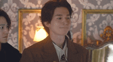 a man in a suit and tie is standing next to another man in a room with a lamp .