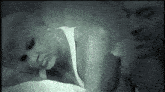 a woman in a white tank top is laying on a bed with a man in the background .