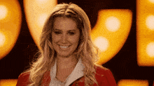 a woman in a red jacket smiles in front of a sign that says ' r '