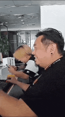 two men are sitting at a table looking at their cell phones .
