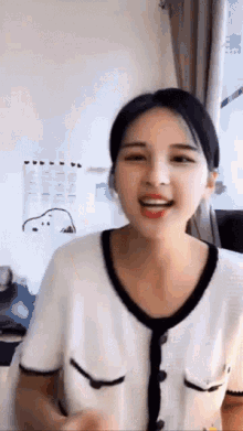 a woman wearing a white shirt with black trim is smiling