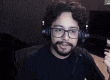 a man with a beard and glasses is wearing headphones and looking at the camera .
