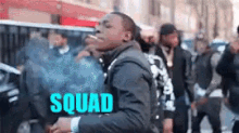 a man is smoking a cigarette in front of a crowd of people and the word squad is on the bottom of the image .
