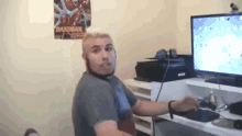 a man sitting in front of a computer with a bakugan poster on the wall above him