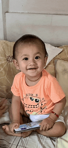 a baby wearing an orange shirt with a monster on it is smiling