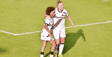 two female soccer players on a field with one wearing a barmenia shirt