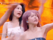 two women are standing next to each other with their arms in the air . one of the women has purple hair .