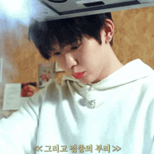a young man in a white hoodie is cooking in a kitchen with asian writing on the bottom