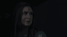 a woman in a blue shirt is standing in a dark room looking at the camera .