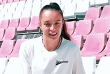 a woman wearing a white shirt that says she got the vote smiles in front of pink and white seats