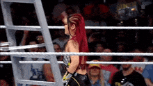 a woman with red hair is standing in a wrestling ring with a crowd watching .