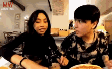 a man and a woman are sitting at a table with a pizza in front of them and the word mw is on the bottom right