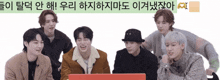 a group of young men are sitting around a laptop with korean writing on the bottom right