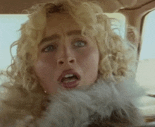 a woman with curly blonde hair is sitting in a car with her mouth open .