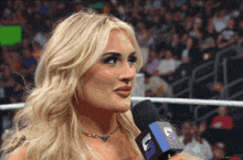 a blonde woman is talking into a microphone with the letter k on the top