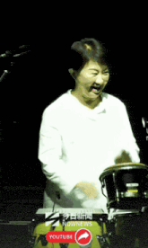 a woman in a white shirt is playing drums in front of a youtube button