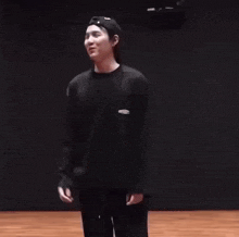 a young man wearing a black hat and a black sweater is dancing on a stage .