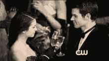 a black and white photo of a man and a woman toasting with wine glasses .
