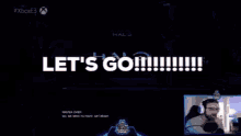 a screen says let 's go while a man stands in front of a microphone