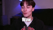a young man in a black hoodie is making a funny face with the words waw written on his face .