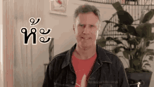 a man wearing a denim jacket and a red shirt is smiling in front of a plant .