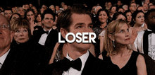 a man in a tuxedo is sitting in a crowd with the word loser above him