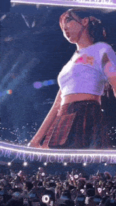 a woman in a crop top and plaid skirt is standing on a stage in front of a crowd of people .