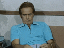 a man in a blue shirt is sitting on a couch reading a book