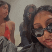 a woman wearing sunglasses looks at the camera while two other women look on