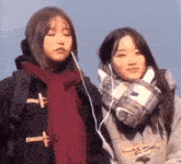 two young women wearing scarves and ear buds are standing next to each other