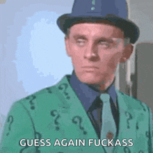 a man wearing a green jacket with question marks on it and a hat says guess again fuckass